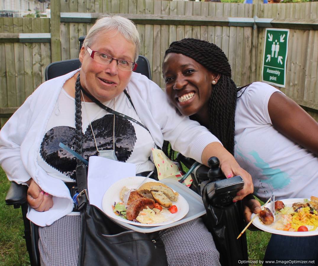 Two women eating food at GIG meeting in a garden.
