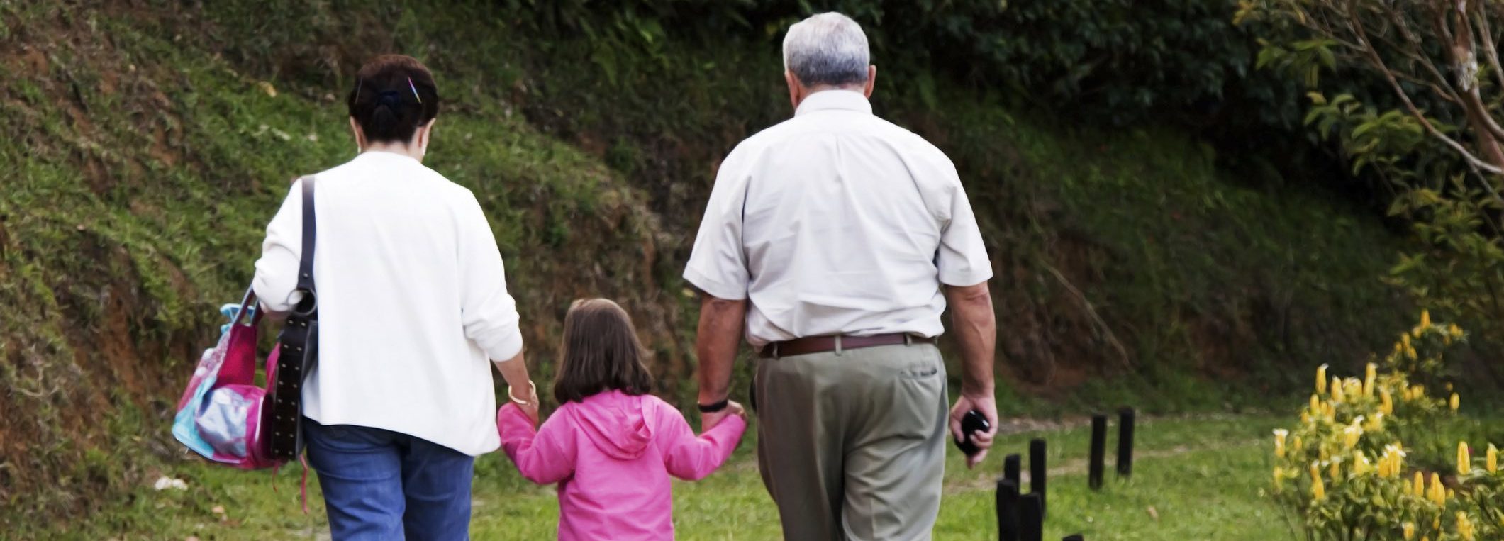 grandparents holding hands with child, walking away from camera