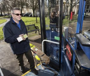 Image of sight impaired man with assistance dog entering a bus