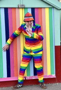 Photo of man in striped suit hiding in front of striped painted beach hut