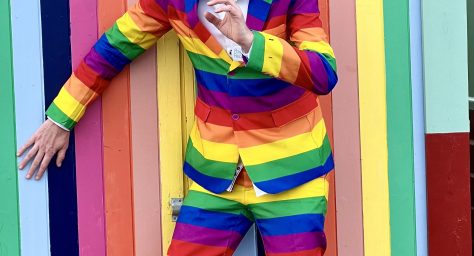 Photo of man in striped suit hiding in front of striped painted beach hut