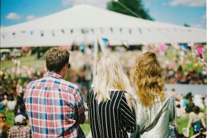 3 people stand with their backs to the camera. They are looking at a marquee strung with colourful bunting.