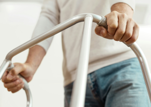a close up shot of a man in a white jumper and jeans leaning on a silver walking frame