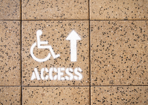 brown speckled floor tiles with a disabled access sign spray painted on in white with an arrow pointing up