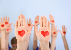 a group of raised hands with red hearts painted on the palms, against a blue background