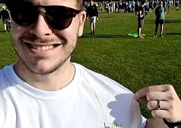 A smiling man wearing sunglasses squints at the sun. He is wearing a Possability People tshirt. Behind him we see a large park with lots of people wearing running clothes.